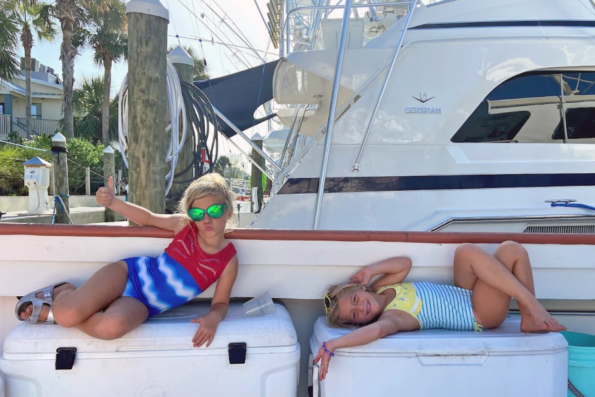 two girls sunbathing on back deck of offshore fishing boat docked at orange beach marina