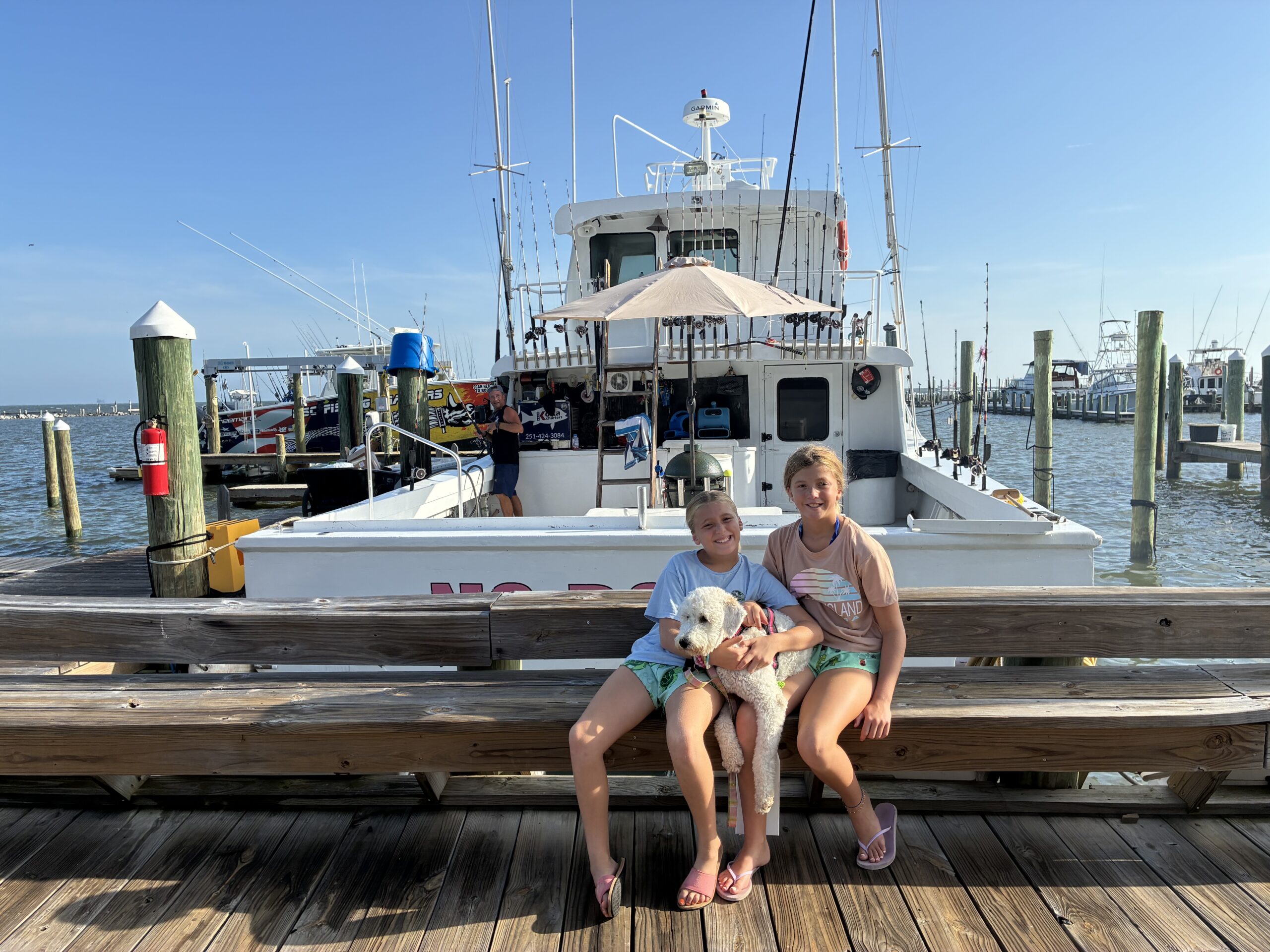 girls sitting in front of No Doubt charter fishing boat at dock at Fort Morgan Marina